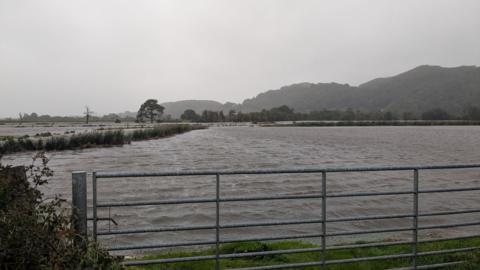Water has completely covered a farmers field. The water stretches off across the whole of the field and stops just before a metal gate, leaving the scene looking like a giant lake.