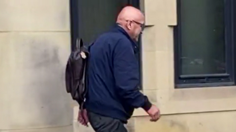 Dr Alexander Zarneh leaving court dressed in black trousers and a blue jacket. He is a bald, elderly man.