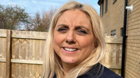 Woman with blonde hair smiling near an outside fence.