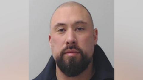 Jonathan Moroney looks at the camera in a police mugshot, he has a beard.