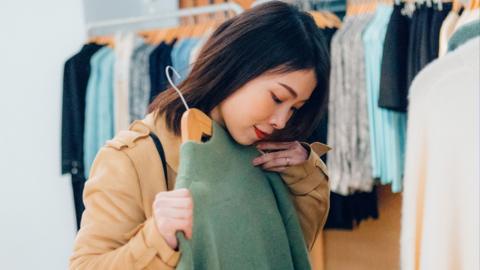 A young woman holds a green jumper in front of herself in a clothes shop