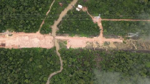 A drone shot of a road being dug through the green trees of the Amazon rainforest