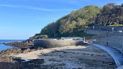 A landscape of the former sight of the restaurant in the background is the sea as well as some trees and roads 