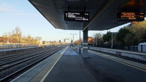 Looking down a platform at Oxford Railway Station. The platform is empty with electronic signs hanging from the roof showing the next service.