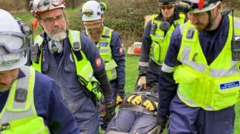 Volunteers dressed in high-vis and helmets carry someone on a stretcher