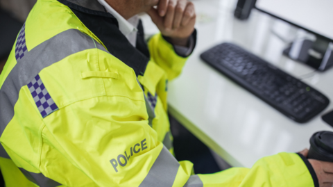 Anonymous picture of a police officer looking at a computer in a police station 