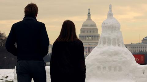 Visitors look at a snow sculpture of the U.S. Capitol building with the actual Capitol in the background, decorated with flags for the upcoming inauguration of U.S. President-elect Donald Trump