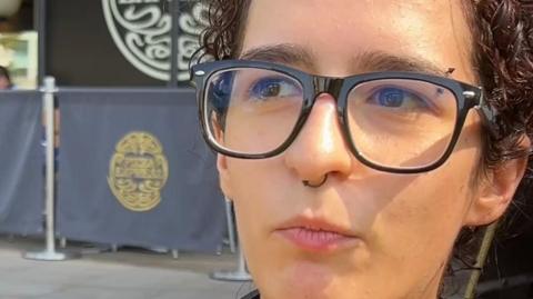 Young woman wearing glasses and a nose ring stands outside