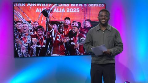 De-Graft in the studio with the Lions rugby team in the screen