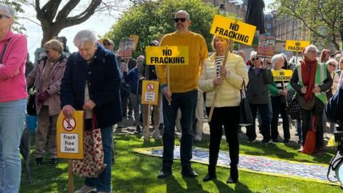 A group of people hold signs reading "no fracking" and "frack free zone".