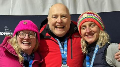 Neil is standing between two women. On the left of the picture is Cath Pendleton, the first woman to swim a kilometre inside the Arctic Circle. She is wearing a pink woolly hat and a pink jacket. She also has a large pair of glasses.
On the left of the picture is Karen Mee from Kenilworth, who is wearing a multi-coloured woolly hat and a blue gilet over a grey top.