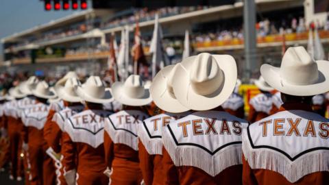 The Texas Longhorns band, wearing shirts with 'Texas' on the back and cowboy hats, on the track before the United States Grand Prix in 2024