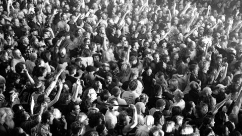 A black and white photo of a crowd of people tightly packed together at a concert, which is being used as part of Idles' promotioanl material for their War Child concert.