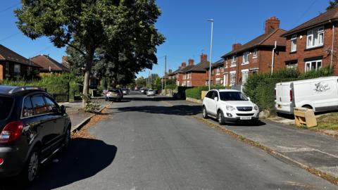 A general view of Sherwin Street in Stoke-on-Trent - a residential street with cars parked on both sides and a tree on the pavement to the left.