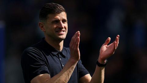 Portsmouth manager John Mousinho claps fans in dark blue polo shirt