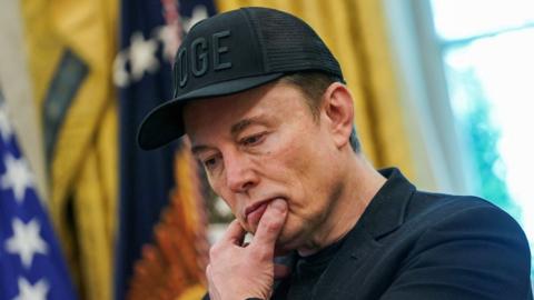 Elon Musk looks pensive while standing in the Oval Office
