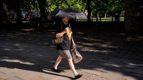A woman walking through Queen's Square in Bristol is holding a parasol