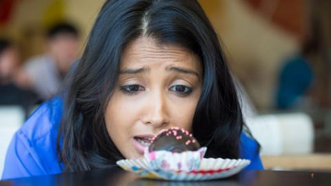 A woman stares longingly at a chocolate cake