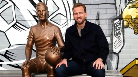 Harry Kane sat next to his statue at Peter May Sports Centre in London.