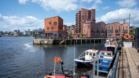 A CGI of how the Malmo development could look. There are a number of apartment buildings built on the land at the mouth of the Ouseburn and overlooking the River Tyne. Small fishing boats can be seen in the foreground. The Millennium Bridge can be seen in the distance.