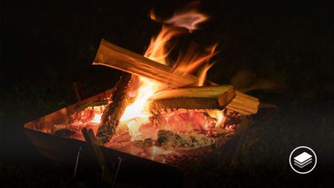 A photograph of a fire with wooden logs on in the dark.