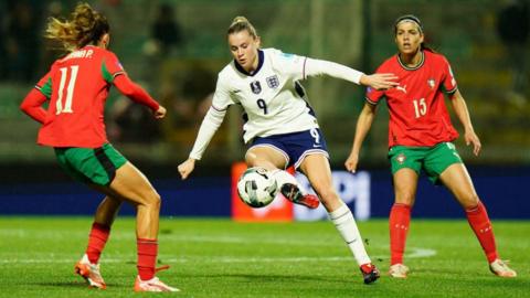 Alessia russo kicking the ball flanked by two italian players