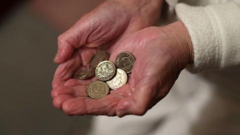 An old woman's hands holding a number of £1 coins