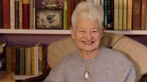 Jacqueline Wilson sits in an armchair in front of bookshelves