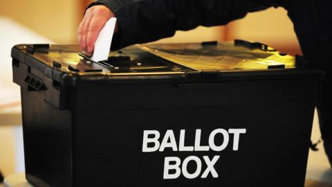 A generic image of a person's arm and hand pushing a ballot paper into a black box with the word "ballot box".