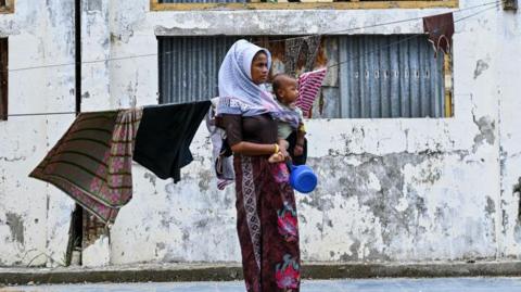 A Rohingya refugee carries her child as she stands at a temporary shelter at a government building in Banda Aceh on December 30, 2023