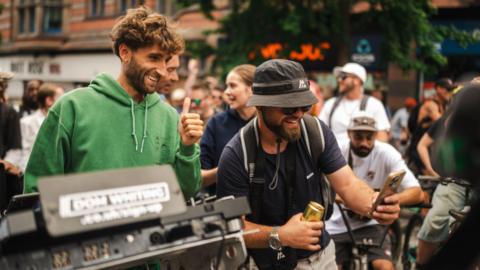 DJ Dom Whiting gives a thumbs up to a rider taking a selfie