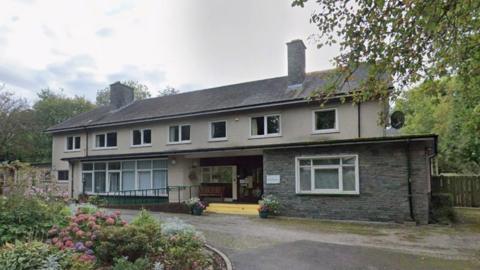 Applethwaite Green Care Home. It is an aging two-storey building. There are flowers in the garden outside the building.