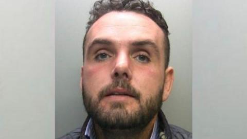 Mugshot of Terry McGinlay who has curly short brown hair and stubble. He has blue eyes and is wearing a Barbour farming style coat. 