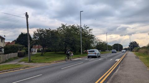 Barwick Road in Crossgates, Leeds, with a cyclist using the left hand side along with other traffic. 