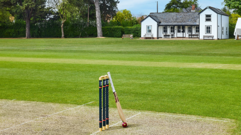 A view of a cricket pitch at Woodbridge School. Cricket stumps rest on the green along with a cricket bat and ball.