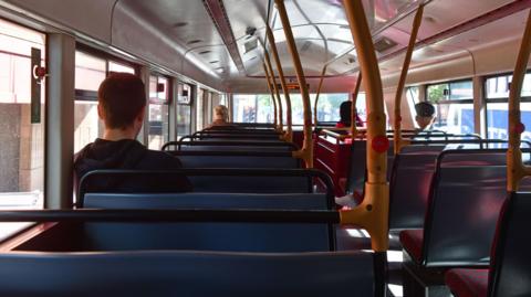 An empty looking bus, with people sat far apart. Taken from the back seat of a bus.