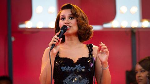 A woman in a black dress. She is performing at a concert.