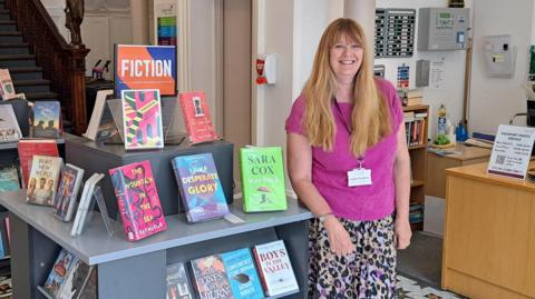 Woman in purple top and skirt stood in the Guille-Alles Library 