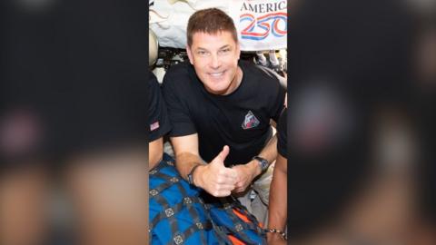Astronaut Jeremy Hansen gives a thumbs up while onboard the Orion spacecraft. He is wearing a dark blue T-shirt.