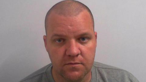 Michael Watt's mugshot - a bald man with blue eyes and a grey sweatshirt.