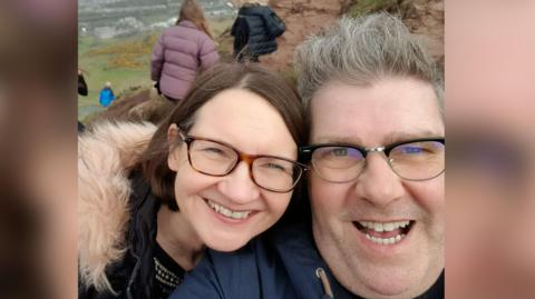 Sandra O'Hagan and David Burgess are both smiling while pictured outdoors and wearing coats in this selfie.