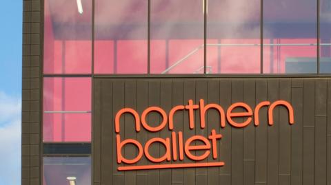 A brown office building with 'Northern Ballet' written in orange signage. Below a sign reads: Phoenix Dance Theatre. 