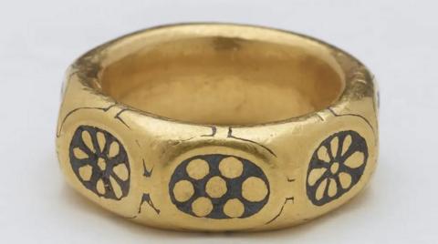 A chunky gold ring with a black circular pattern repeated three times on its side.