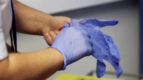  A photo of a man's arms, he is putting on latex gloves.