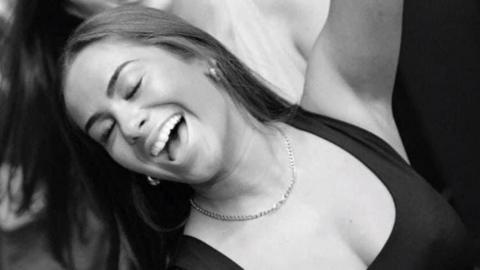 A woman smiling with her eyes closed and arms raised in a black and white photograph