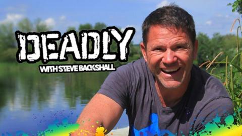 Deadly with Steve Backshall, Steve is an older man wearing a grey shirt and smiling, he is by a large river on a sunny day.