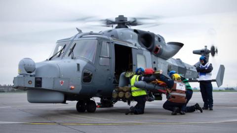 A Wildcat Helicopter being attended to by crew on a runway with its propellers spinning