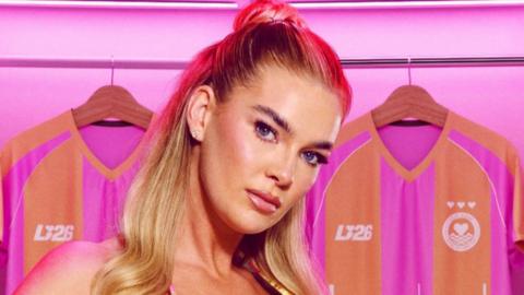 Robyn Langton, who is wearing a bikini, is standing in a changing room surrounded by pink and orange football shirts