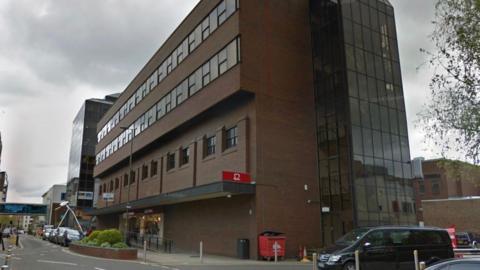 A Google Maps image of the former BHS site in Woking town centre. There is a large brown building with a road in front. 