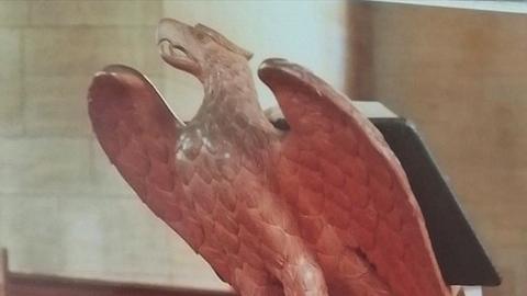 A wooden eagle animal carving atop a lectern, with an open book on its back 